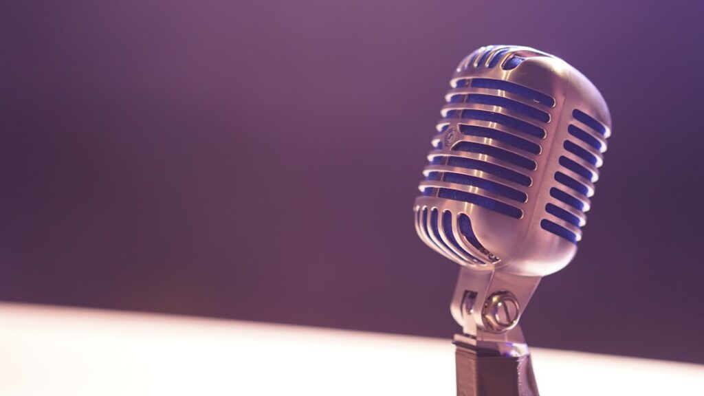A vintage silver microphone with blue accents against a soft purple background